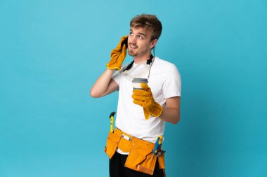 Genç elektrikçi, izole olmuş bir duvarın üzerinde kahve ve bir cep telefonu tutuyor.