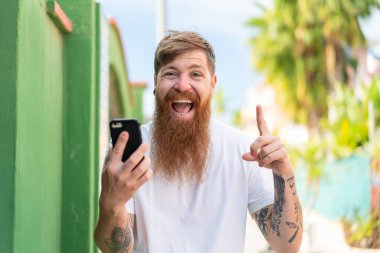 Kızıl saçlı, sakallı, açık havada cep telefonu kullanan harika bir fikir.