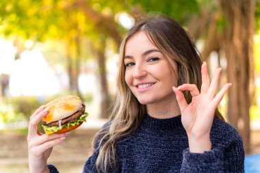 Genç, güzel Romen kadın elinde burgerle gezerken parmaklarıyla 