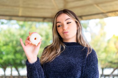 Genç, güzel Romen kadın, elinde üzgün bir ifadeyle dışarıda donut tutuyor.