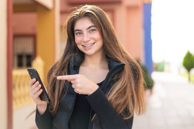 Açık havada cep telefonu kullanan güzel beyaz bir kadın.