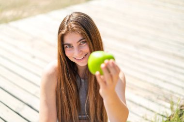 Genç, güzel, beyaz bir kadın elinde mutlu bir ifadeyle bir elma tutuyor.