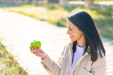 Dışarıda elmalı genç bir kadın, neşeli bir ifadeyle.