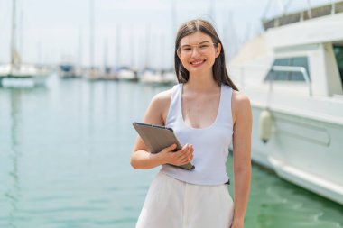 Genç, güzel Ukraynalı bir kadın açık havada elinde tabletle gülümsüyor.