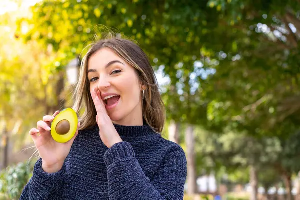 stock image Young pretty Romanian woman holding an avocado at outdoors whispering something