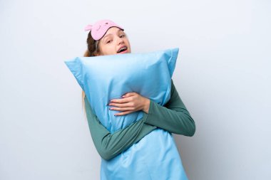 Genç Rus kız pijamalarıyla beyaz arka planda izole edilmiş ve elinde mutlu bir ifadeyle bir yastık tutuyor.