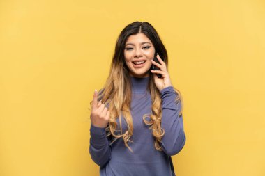 Sarı arka planda izole edilmiş cep telefonu kullanan genç Rus kız geliyor.