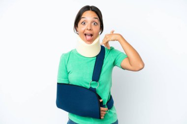 Beyaz arka planda izole edilmiş boyunluk takan ve askı takan İspanyol genç bir kadın telefon jesti yapıyor. Bana geri dönüş işareti ver.