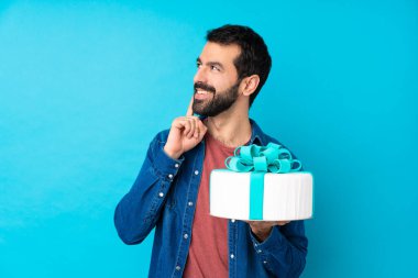 Büyük pastası olan genç yakışıklı bir adam mavi arka plan üzerinde bir fikir düşünürken yukarı bakıyor.