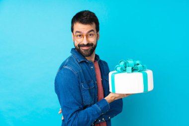 Gözlüklü ve gülümseyen, soyutlanmış mavi arka planda büyük bir pastası olan genç yakışıklı bir adam.