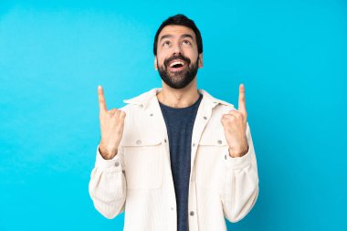 Beyaz kadife ceketli genç ve yakışıklı bir adam izole edilmiş mavi arka planda şaşırmış ve yukarı bakıyor.