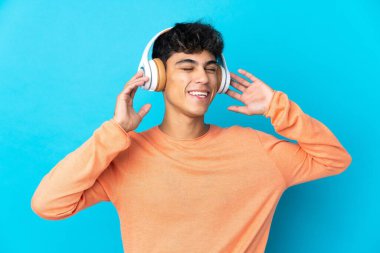 Genç adam soyutlanmış mavi arka plan müzik dinliyor ve şarkı söylüyor.