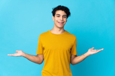 Venezuelalı genç adam mavi arka planda izole edilmiş ve şok olmuş bir yüz ifadesi var.