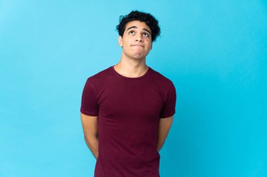 Genç Venezuelalı adam mavi arka planda izole edilmiş ve yukarı bakıyor.