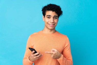 Venezuelalı adam mavi arka planda cep telefonu kullanarak izole edilmiş.