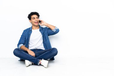 Venezuelalı adam yerde oturuyor ve cep telefonuyla sohbet ediyor.