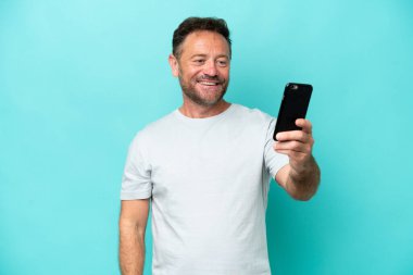 Middle age caucasian man isolated on blue background making a selfie