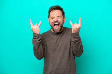 Middle age caucasian man isolated on blue background making horn gesture