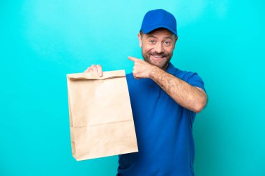 Orta yaşlı bir adam mavi arka planda izole edilmiş bir paket yiyecek alıyor.