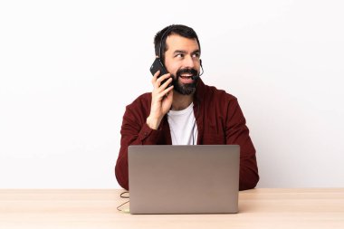 Tele-pazarlamacı beyaz adam kulaklıkla ve dizüstü bilgisayarla çalışıyor cep telefonuyla sohbet ediyor..