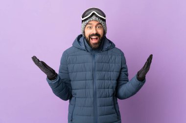 Kar kaykayı gözlüklü kayakçı, mor arka planda, şok olmuş yüz ifadesi var.