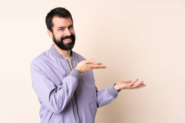 Sakallı, ceketli, soyutlanmış arka planda beyaz bir adam. Davet etmek için ellerini yana uzatıyor.