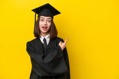 Genç üniversite mezunu Ukraynalı kadın sarı arka planda izole edilmiş şaşırmış ve işaret ediyor.