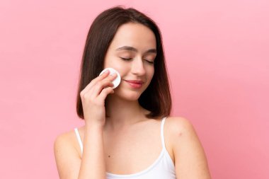 Young Ukrainian woman isolated on pink background with cotton pad for removing makeup from her face