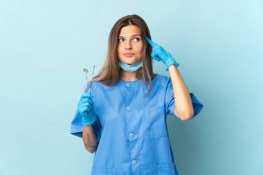 Slovak dişçi mavi arka planda izole araçlar tutuyor şüpheleri ve düşünceleri var