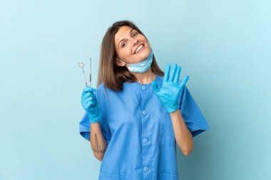 Slovak dişçi mavi arkaplan üzerinde izole araçlar tutuyor mutlu ifade ile el sallama