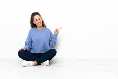 Genç bir kadın yerde oturuyor ve parmağıyla işaret ediyor.