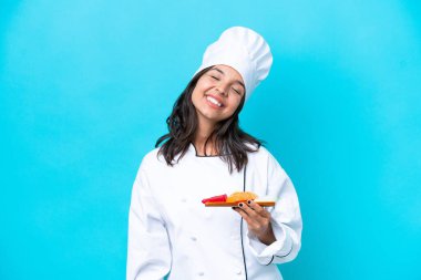 Genç İspanyol aşçı kadın elinde sashimi ile mavi arka planda izole edilmiş kahkaha atıyor.