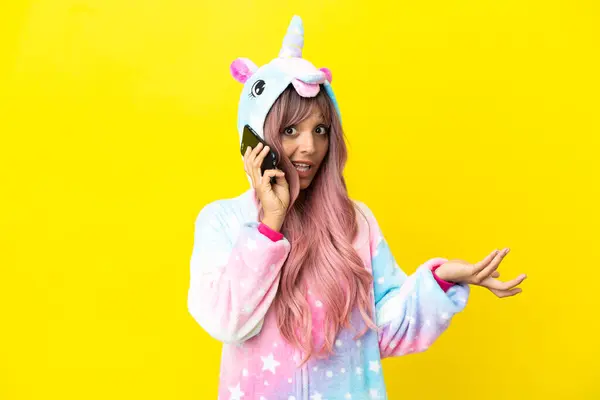 stock image Young mixed race woman wearing a unicorn pajama isolated on white background keeping a conversation with the mobile phone with someone