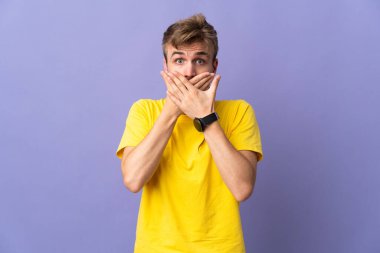 Mor arka planda izole edilmiş genç, yakışıklı sarışın adam elleriyle ağzını kapatıyor.