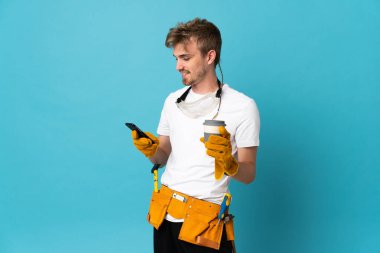 Genç elektrikçi, izole olmuş bir duvarın üzerinde kahve ve bir cep telefonu tutuyor.