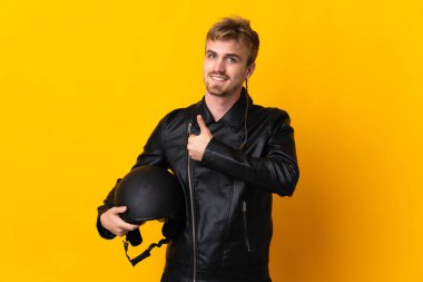 Motosiklet kasklı bir adam sarı arka planda izole edilmiş bir şekilde baş parmak hareketi yapıyor.