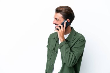 Beyaz arka planda izole edilmiş genç beyaz bir adam cep telefonuyla sohbet ediyor.