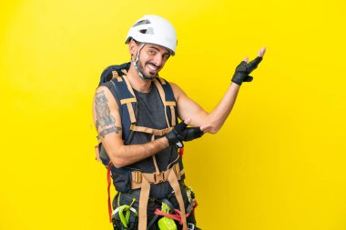 Kafkasyalı genç dağcı, sarı arka planda izole edilmiş. Davet etmek için ellerini yana uzatıyor.