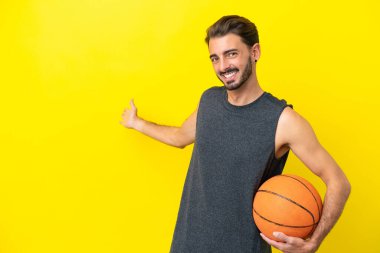 Yakışıklı genç basketbolcu. Sarı arka planda izole edilmiş. Gelmesi için ellerini yana uzatıyor.