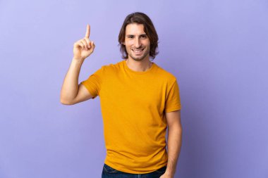 Mor arka planda izole edilmiş genç yakışıklı adam harika bir fikre işaret ediyor.
