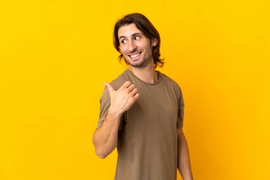 Sarı arka planda izole edilmiş genç yakışıklı bir adam bir ürün sunmak için kenarı işaret ediyor.