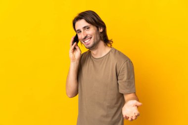 Sarı arka planda izole edilmiş genç ve yakışıklı bir adam cep telefonuyla sohbet ediyor.