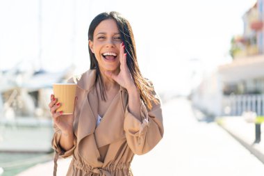 Dışarıdaki genç kadın açık havada kahvesini yudumlarken ağzı açık bağırıyordu.