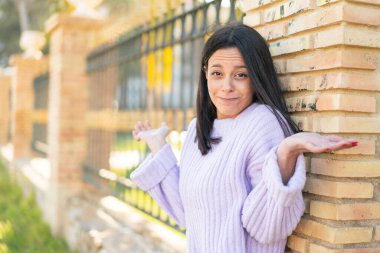 Dışarıda el kaldırırken kuşkuları olan genç bir kadın.