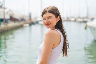 Genç, güzel bir kadın açık havada, mutlu bir ifadeyle.