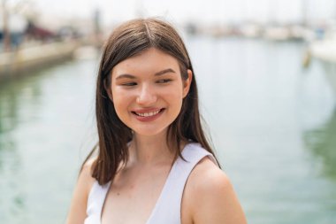 Genç, güzel bir kadın açık havada, mutlu bir ifadeyle.