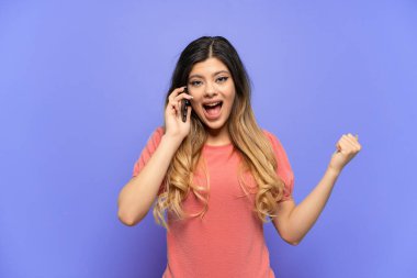 Genç Rus kız mavi arka planda izole edildi. Baş parmak kullanırken cep telefonu kullandı.