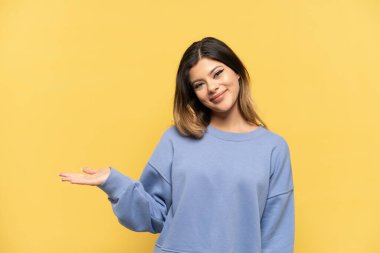 Sarı arka planda izole edilmiş genç Rus kız gülümserken bir fikir sunuyor.