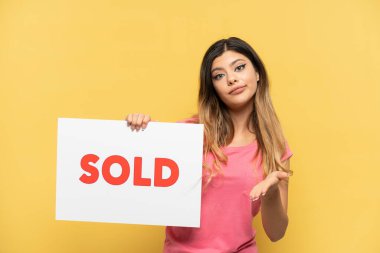 Sarı arka planda izole edilmiş genç bir Rus kız. Elinde bir pankart var ve anlaşma yapıyor.