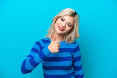 Mavi arka planda izole edilmiş genç bir Rus kadın baş parmak işareti yapıyor.